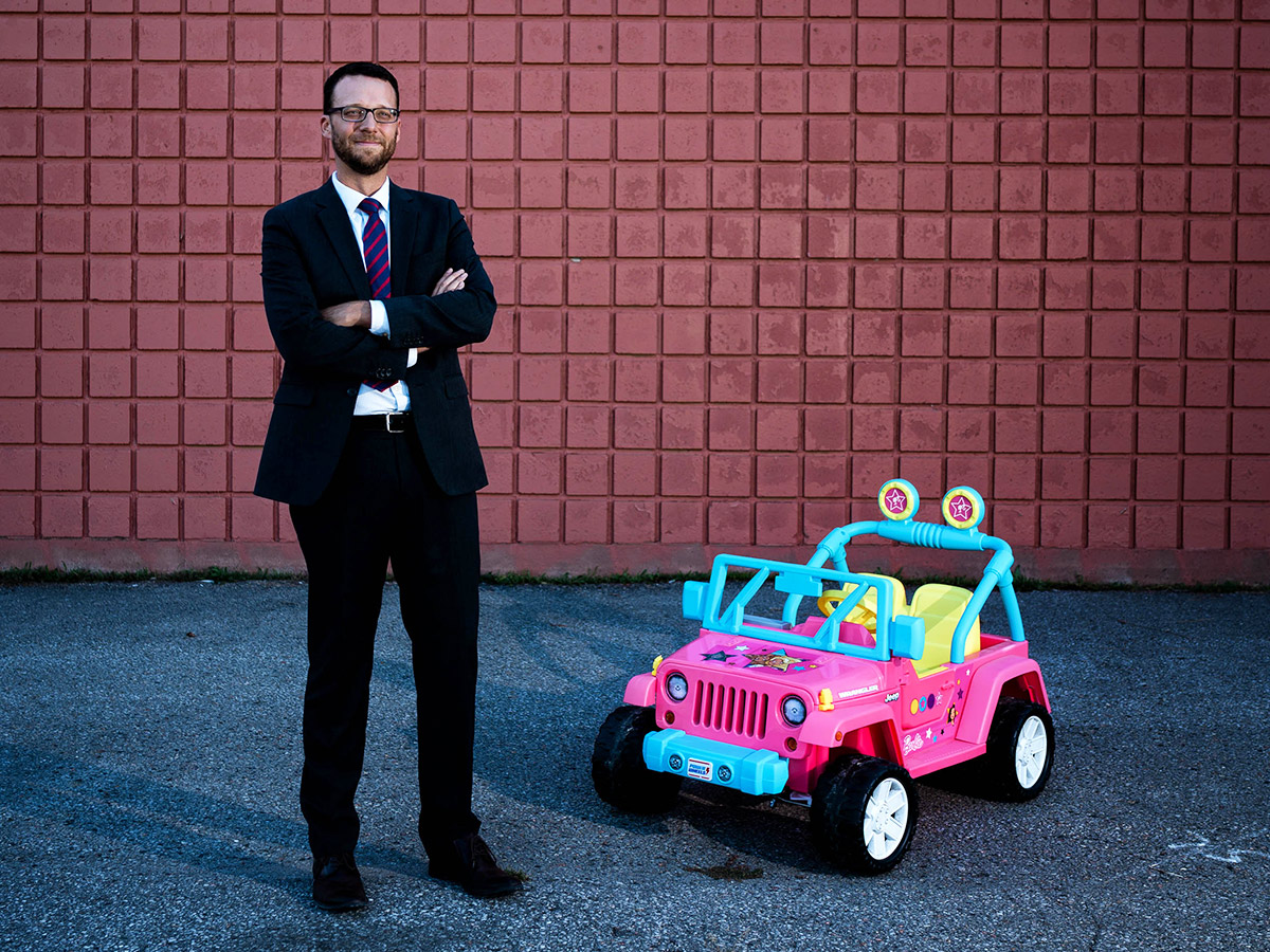picture of suited man standing next to a toy pink jeep